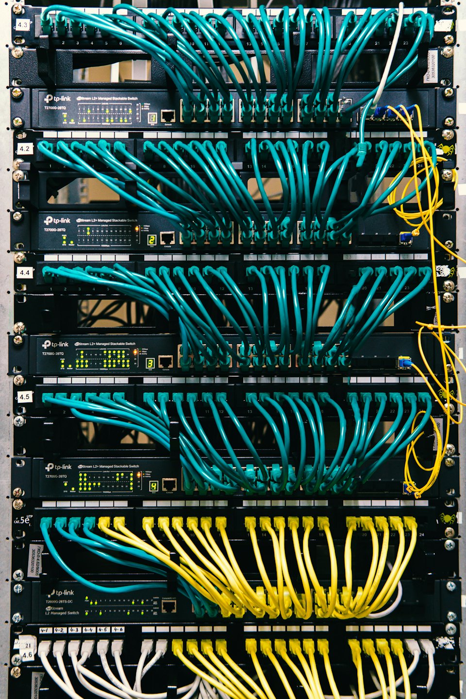 Server rack with many teal and yellow Ethernet cables.